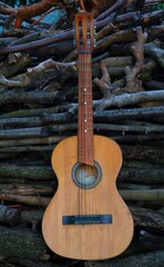 Rustic guitar in front of stacked wood logs. A weathered acoustic guitar leaning on stacked firewood outdoors. Ideal for rustic lifestyle visuals, outdoor music themes, or storytelling ima