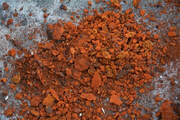 Rust chips on concrete. Crushed red clay on a concrete background. Vibrant crushed red clay or brick powder on grey concrete. Great for creating textures in design, visualising raw materials or creati