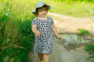 A small child strolls down a countryside path wearing a comfortable dress and a cute hat The...