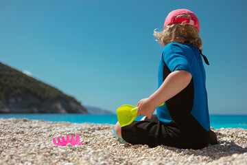 Young child playing with colorful beach toys on Mediterranean pebble beach in summer