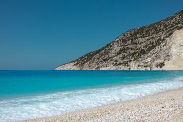 Fototapeta premium Turquoise Mediterranean waves gently washing onto white pebble beach with limestone cliffs