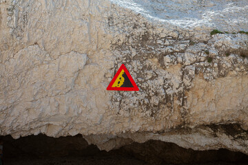 Red triangular warning sign with falling rocks symbol on weathered limestone cliff face