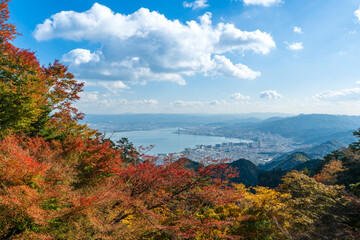 High-angle view of Lake Biwa framed by vibrant autumn maple foliage from the Mount Hiei against a blue sky. Otsu, Shiga, Japan.
