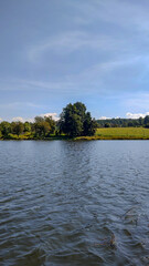 Beautiful view of a lake, with fresh, blue water, and a field with trees, in spring on a sunny day.