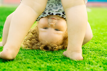 A young girl with curly hair enjoys a playful moment outside doing a handstand on bright green...