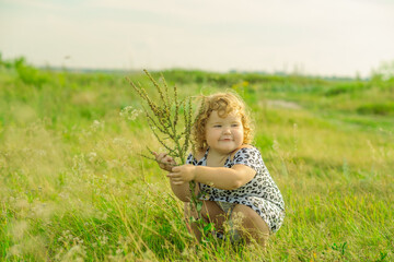 A joyful young girl sits in a lush green field playing with plants The sun shines brightly as she...