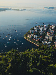 Aerial view of Rio de Janeiro&rsquo;s coastline with boats anchored near the shore, vibrant buildings, lush green trees, and a wide expanse of sky under beautiful morning light.

