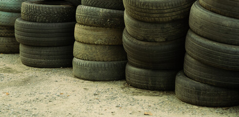 Stacks of assorted used tires rest against a wall at a recycling facility showcasing varying sizes...