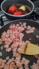 Preparing breakfast at home in the morning: frying diced ham with oil and cooking some tomatoes, onion, garlic, and chilies for a sauce.