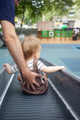 Father supporting toddler boy sitting on slide at outdoor playground during summer day — bonding, parenting and child safety concept