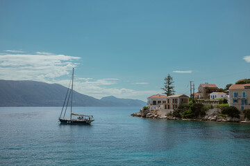 Elegant sailboat anchored in crystal clear waters near traditional Greek island architecture.