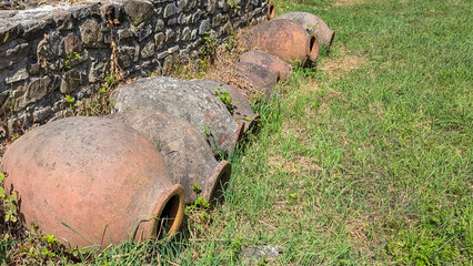 Weathered qvevri ceramic wine vessels resting against rustic stone wall, highlighting georgian...
