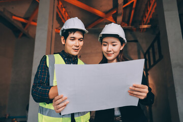 Construction manager and engineer dressed in orange work vests and hard helmets explore...