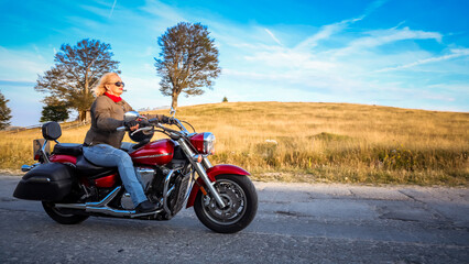 Fototapeta premium Confident woman riding a red cruiser motorcycle through the countryside on a sunny day, enjoying freedom and open road in golden light.