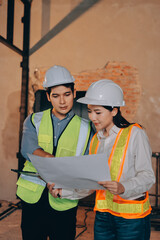 Construction manager and engineer dressed in orange work vests and hard helmets explore...