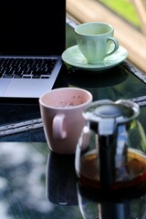 Kubek, filiżanka i komputer na stole - praca w domu. Praca i biznesowy klimat. Zdalna praca.