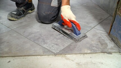 Construction worker applying grout between tiles using rubber grout float