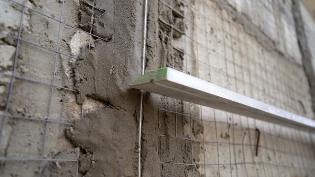 Construction worker plastering a wall using metal lath and a long leveling tool for a smooth finish