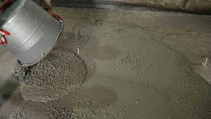 Construction worker pouring concrete mix from a bucket, skillfully creating a new floor at a building site during renovation work