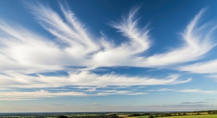 Wispy cirrus clouds stretch across a blue sky over rolling hills