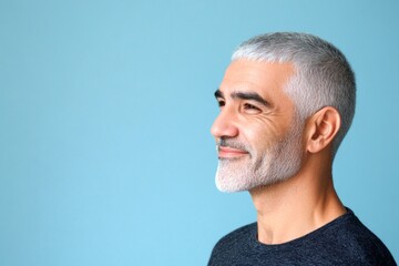 Fototapeta premium A gentle smile lighting up a maleâ€™s face. Trendy men's hard part haircut - midlife middle eastern man with short hair. Concept pattern art of style for aging men. Blue solid background.