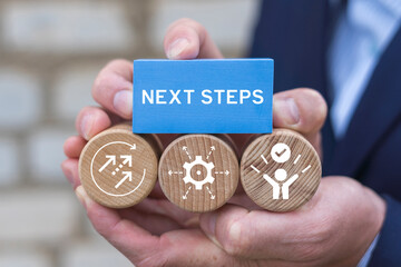 Business person holding blocks with icons sees the inscription: NEXT STEPS. Next Steps Business Progress Development Career Concept.
