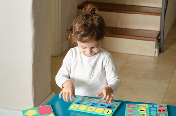 A little girl playing with colorful foam letters, numbers and geometric shapes on a blue table. 