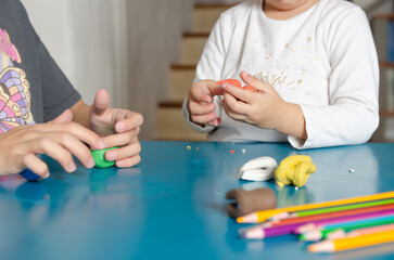 Two little sisters playing with colorful modeling dough on a blue table. 