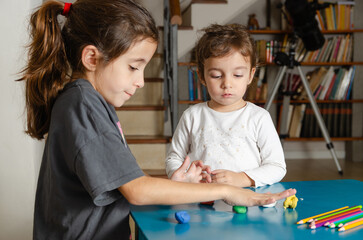 Two little sisters playing with colorful modeling dough on a blue table. 