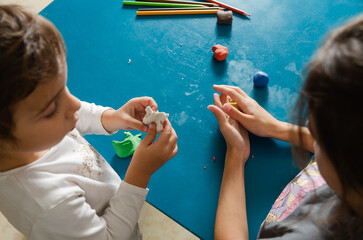 Two little sisters playing with colorful modeling dough on a blue table. 