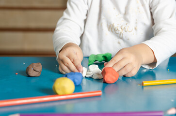 A little girl playing with colorful modeling dough on a blue table.