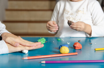 Two little sisters playing with colorful modeling dough on a blue table. 