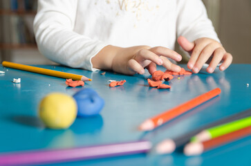 A little girl playing with colorful modeling dough and pencils on a blue table.