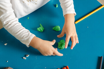 A little girl playing with colorful modeling dough and pencils on a blue table.