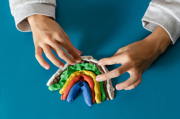 The hands of a young girl making a rainbow with colorful modeling dough.