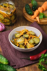 Pickled vegetable salad of cucumbers and carrots in a ceramic bowl on a wooden background. Canning, preparations. Step-by-step recipes.