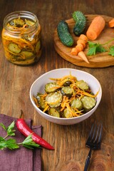 Pickled vegetable salad of cucumbers and carrots in a ceramic bowl on a wooden background. Canning, preparations. Step-by-step recipes.