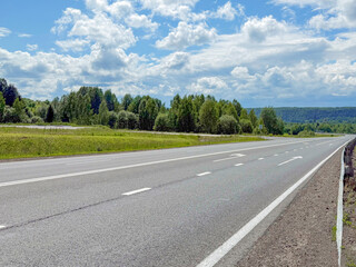 Expansive highway stretches through lush green landscape under a bright blue sky with fluffy clouds, showcasing the beauty of nature and modern infrastructure