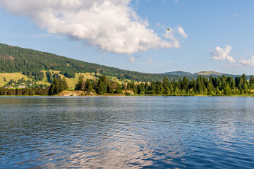Paragliding Over Lac des Rousses in Summer. Landscape of lake, forest and mountain. Les Rousses, Jura, France.