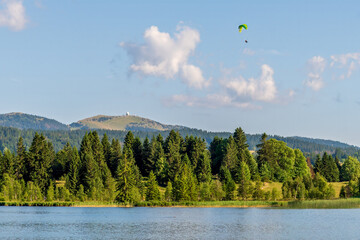 Paragliding Over Lac des Rousses in Summer. Landscape of lake, forest and mountain. Les Rousses, Jura, France.