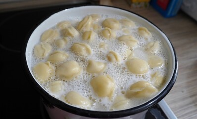 a pot of boiling water in which the dumplings are cooked. The water actively foams and rises to the edges of the pan.