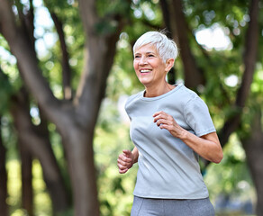 Smiling active mature elderly woman jogging running in the park