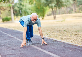 Smiling active senior man standing in start position,  jogging running and walking doing fitness in...