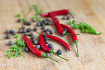 several fresh red chili peppers on a wooden surface surrounded by aromatic peppercorns