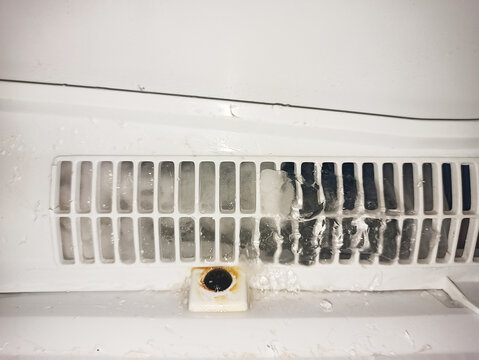 The close-up image shows the back wall of the freezer with a ventilation grate and a drain hole, partially covered with ice and rust. Ice formation and traces of moisture are visible