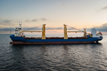Aerial view of a large general cargo ship with deck cranes sailing on the calm open sea against a...