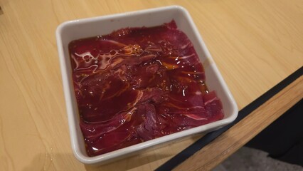 Thinly sliced raw beef marinating in a savory sauce, prepared for grilling or hot pot, presented in a white dish