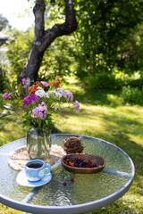 On the glass table there is a vase with bright flowers, a cup of coffee and a vase with assorted...