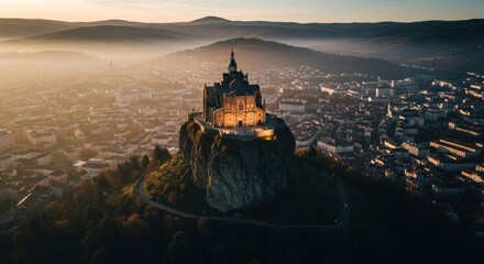 Obraz premium Ornate church atop rocky hill overlooking a hazy cityscape at golden hour
