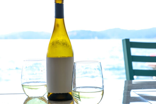 A bottle of white wine with two glasses outside at a lake during a summer vacation. The drink is refreshing and cool during  a hot sunny day. 